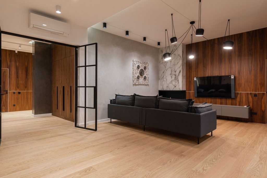 Moderne woonkamer met houten wand, zwarte bank, marmeren accentmuur en designverlichting.